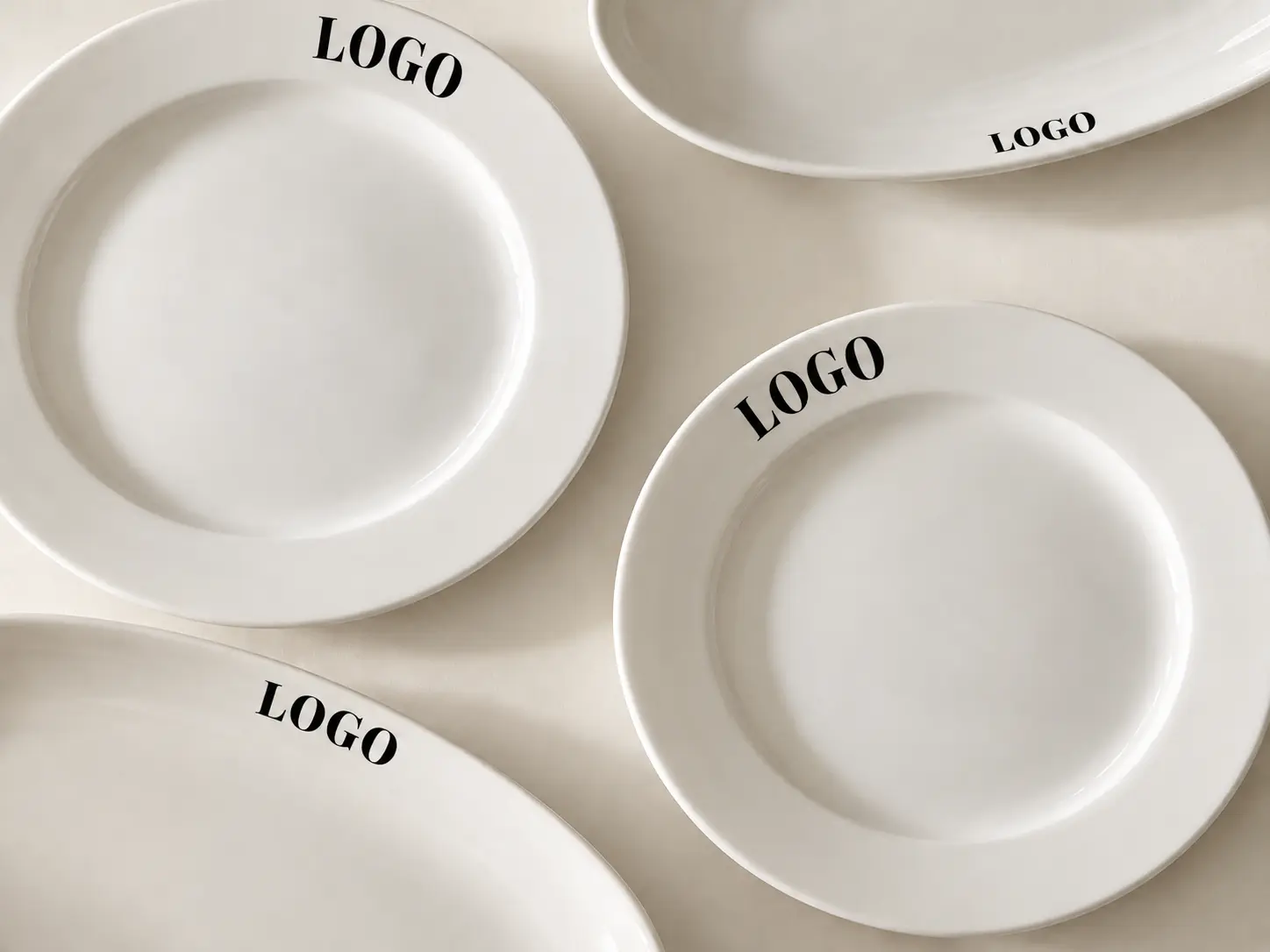 Overhead arrangement of white plates and oval platters with LOGO printed in black on the rims